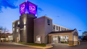 A Sleep Inn by Choice Hotels building with a prominent illuminated sign, a covered entrance, and a parking area. - Sleep Inn Missoula Southgate (Missoula)