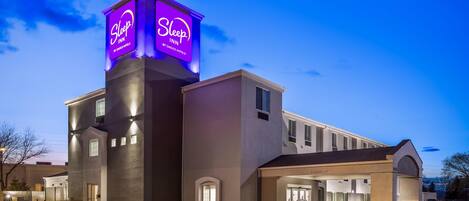 A Sleep Inn by Choice Hotels building with a prominent illuminated sign, a covered entrance, and a parking area.
