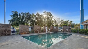 Una piscina rectangular con solárium de hormigón, rodeada de muros de piedra y barandillas metálicas.