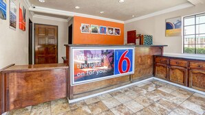 A reception area with a wooden counter, a large sign reading "We'll leave the light on for you.", and a window with a view of greenery.