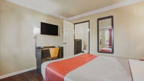 Habitación de hotel con cama, escritorio, silla, televisor y espejo.
