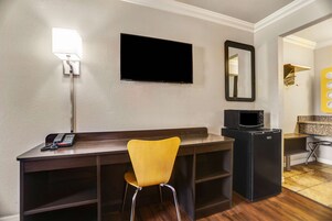 Habitación de hotel con escritorio, silla, televisor de pantalla plana, microondas y refrigerador pequeño.