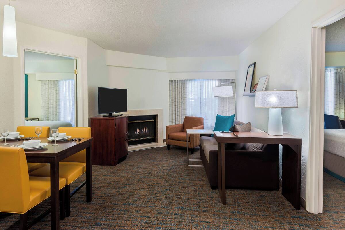 A hotel room with a dining area, a sofa, a TV, a fireplace, and a lamp.