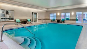 Una piscina interior con agua cristalina, un juego de escalones que bajan a la piscina y varias sillas alrededor de la zona de la piscina.