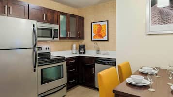 Una cocina moderna con electrodomésticos de acero inoxidable, armarios de madera oscura y un comedor con sillas amarillas y platos blancos.
