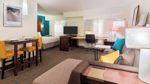 Una habitación de hotel con cama, escritorio con computadora, mesa de comedor con sillas y un sofá.