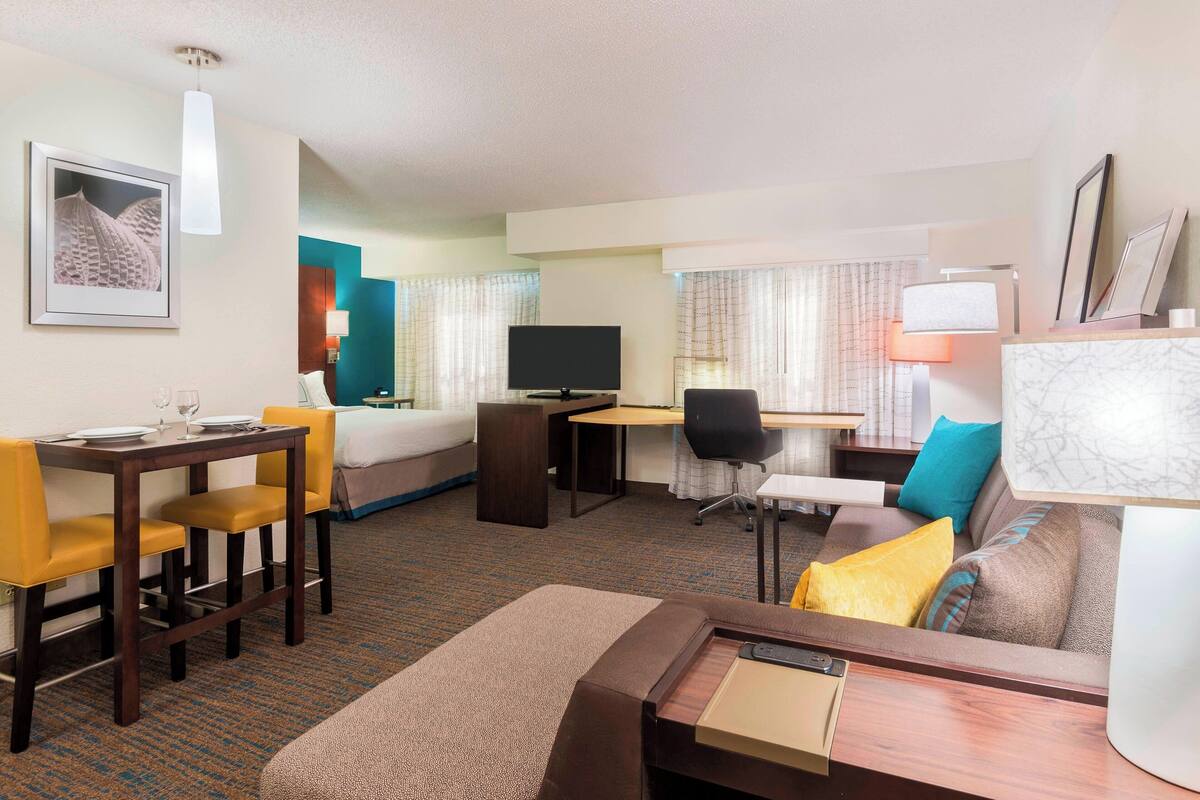 A hotel room with a bed, a desk with a computer, a dining table with chairs, and a sofa.