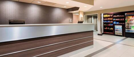 A reception area with a counter, a vending machine, and a refrigerator stocked with beverages.