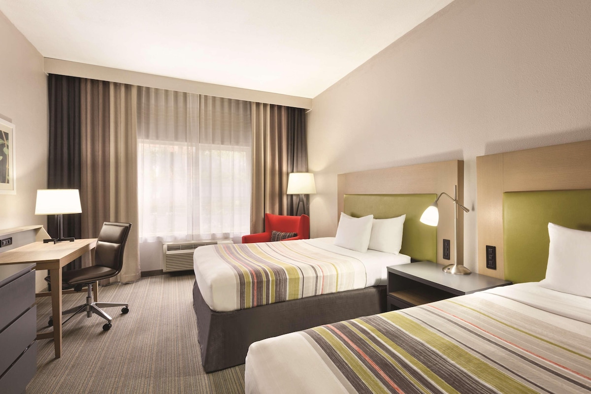 A hotel room with two beds, a desk, a chair, and a window with curtains.
