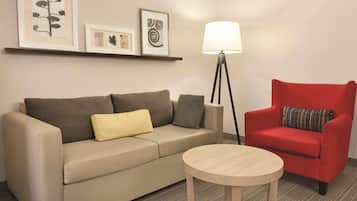 A room with a beige sofa, a red armchair, a small round table, and a floor lamp.