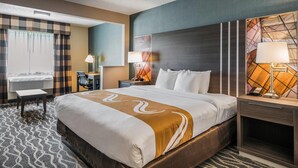 A hotel room with a large bed, a desk, a chair, a lamp, and a window with curtains.