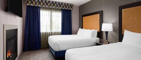 A hotel room with two beds, a TV, a fireplace, and a window with curtains.