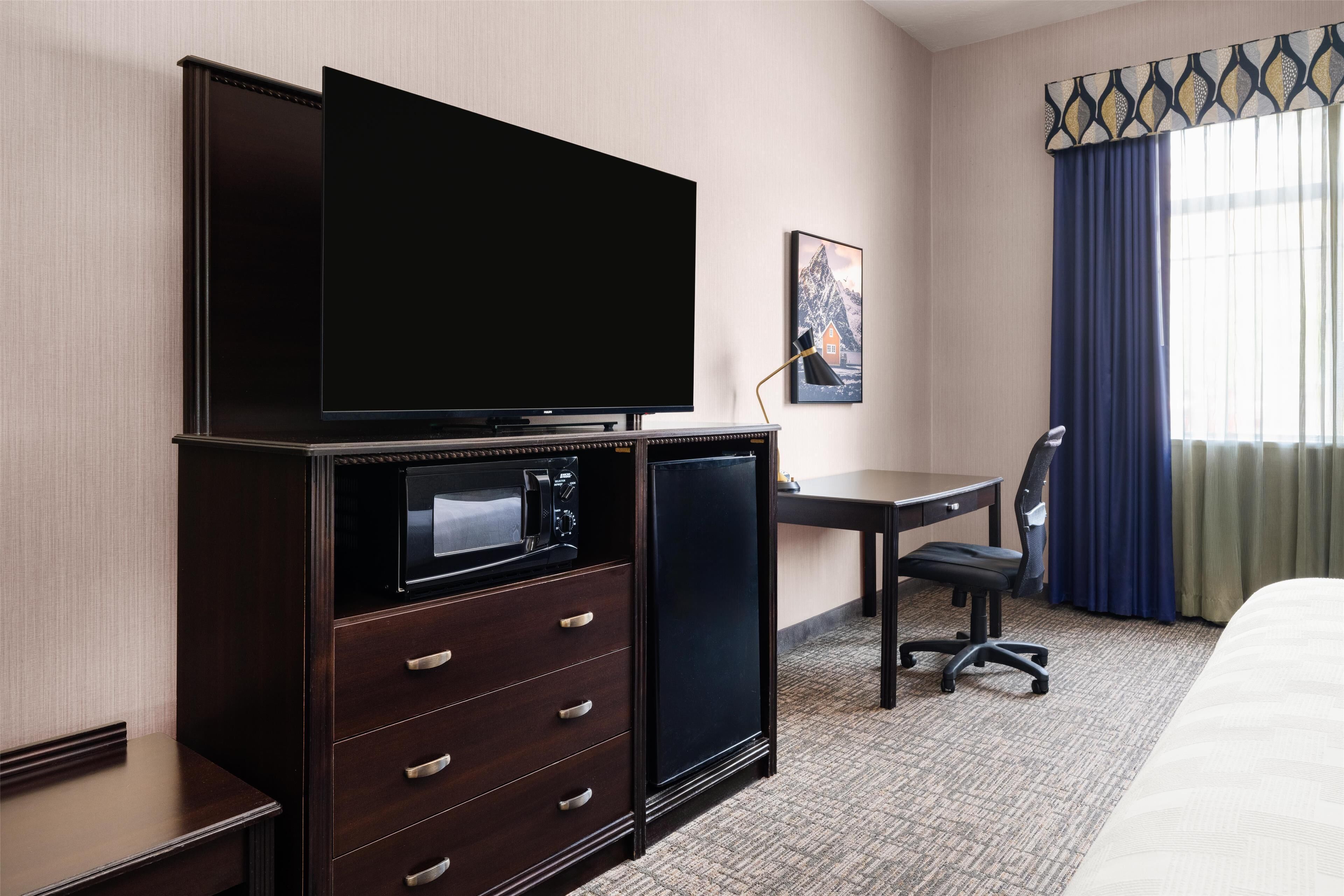 Habitación de hotel con televisión de pantalla plana, refrigerador pequeño, escritorio con silla y una cama.