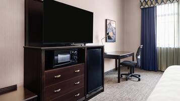 Habitación de hotel con televisión de pantalla plana, refrigerador pequeño, escritorio con silla y una cama.