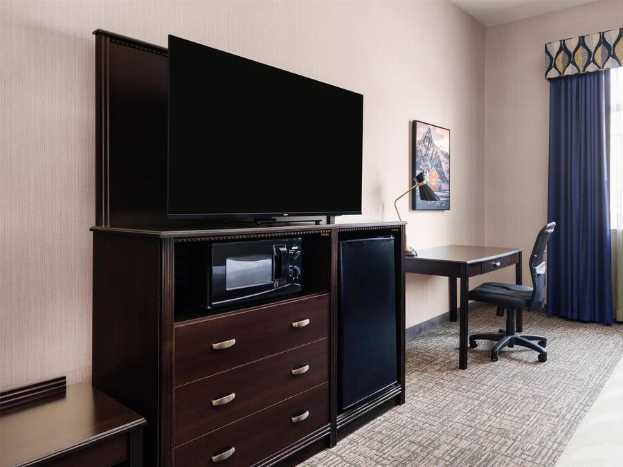 Une chambre d’hôtel équipée d’un téléviseur à écran plat, d’un petit réfrigérateur, d’un bureau avec une chaise et d’un lit.