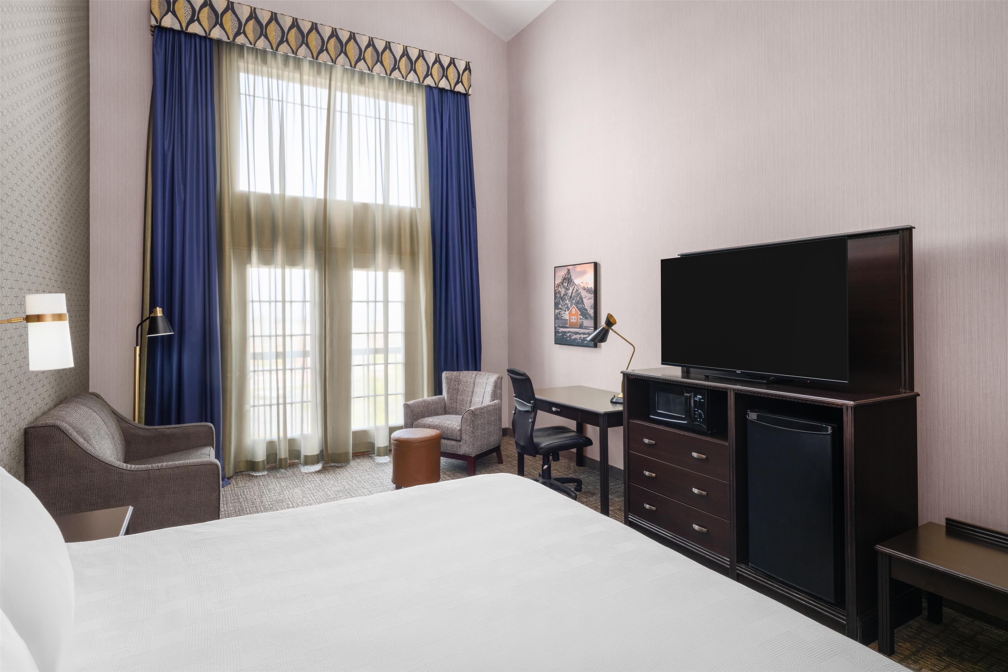 Habitación de hotel con cama, escritorio, silla, televisor y un cuadro en la pared.