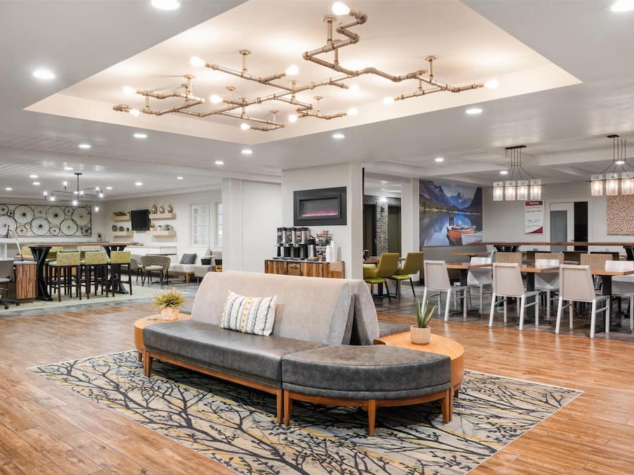 A spacious hotel lobby with a modern design, featuring a central seating area, a dining area, and a bar.