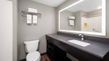 A modern bathroom with a white toilet, a large mirror, and a dark countertop.
