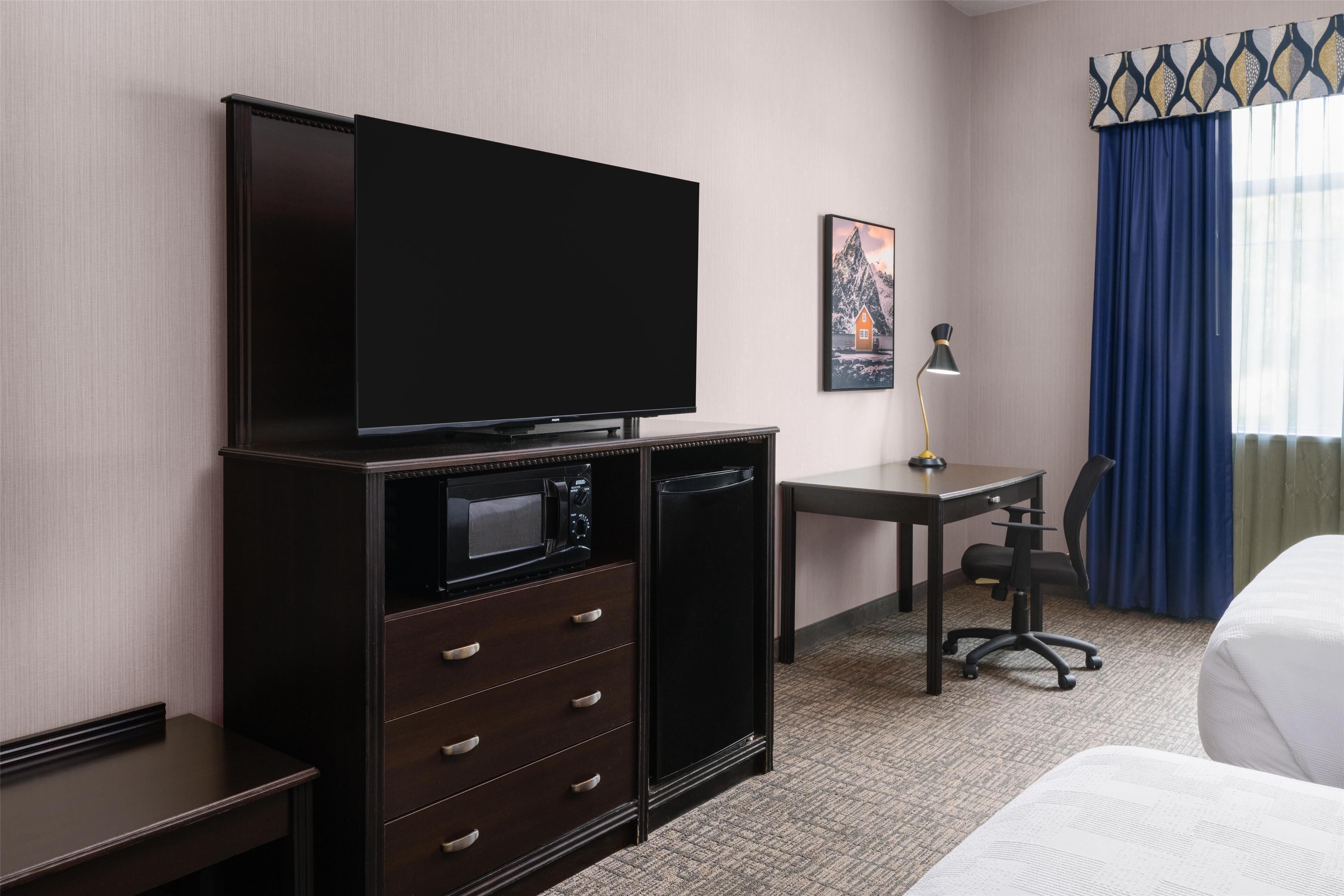 Une chambre d’hôtel équipée d’une télévision à écran plat, d’un bureau avec une lampe, d’une chaise et d’un lit.
