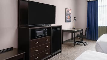 Une chambre d’hôtel équipée d’une télévision à écran plat, d’un bureau avec une lampe, d’une chaise et d’un lit.
