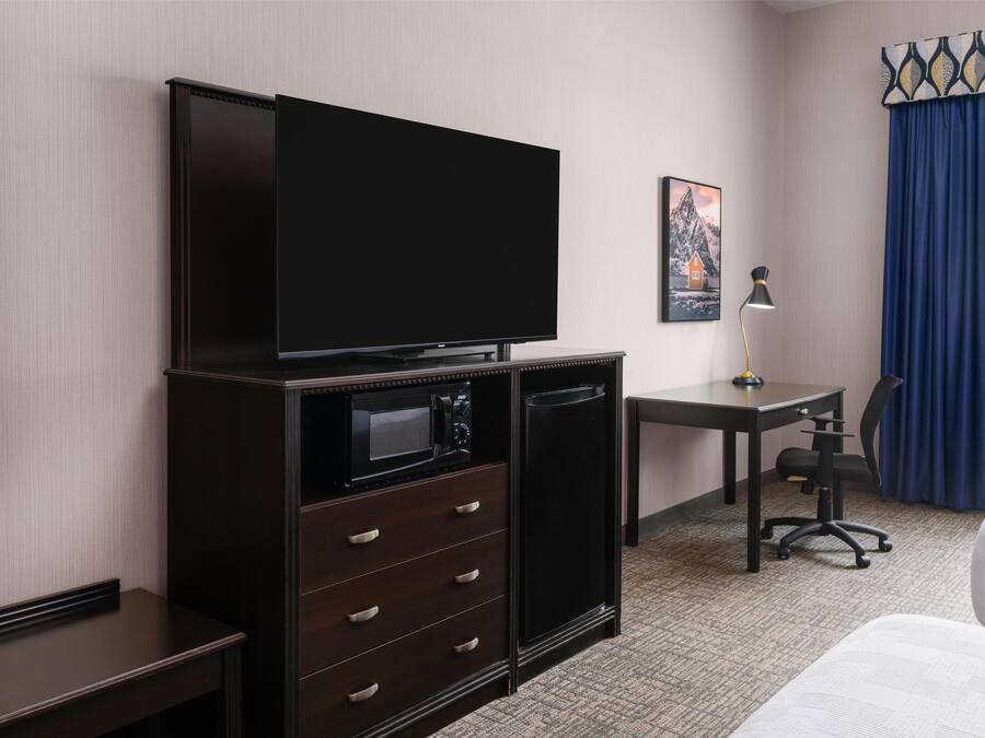 Ein Hotelzimmer mit Flachbildfernseher, Schreibtisch mit Lampe, Stuhl und Bett.
