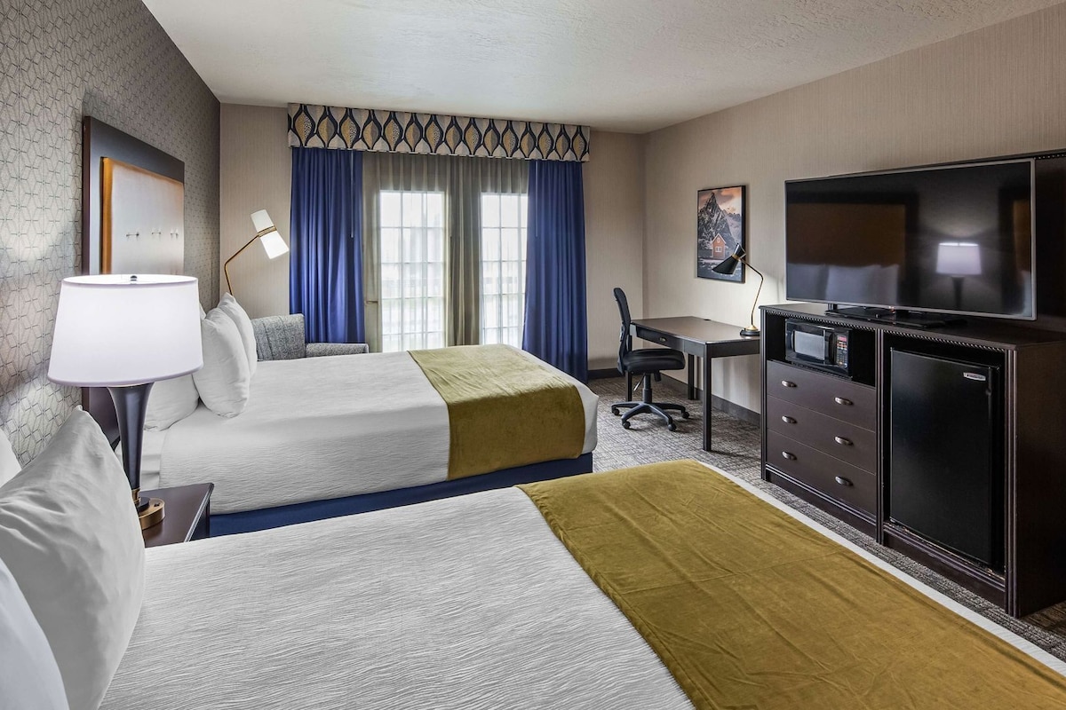 A hotel room with two beds, a desk, a television, and a minibar.