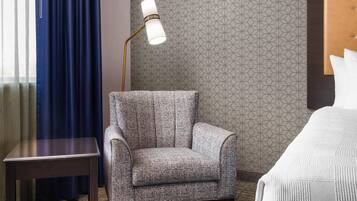 Une chambre d’hôtel avec un mur à motifs, un fauteuil, une table de chevet, une lampe et un lit avec des oreillers.