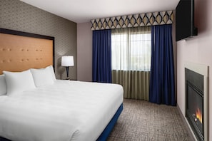 A hotel room with a large bed, a television mounted on the wall, a fireplace, and a window with curtains. - Best Western Plus Grant Creek Inn (Missoula)