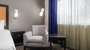 Habitación de hotel con pared estampada, un sillón gris, una mesita, una mesita de noche y una cama.
