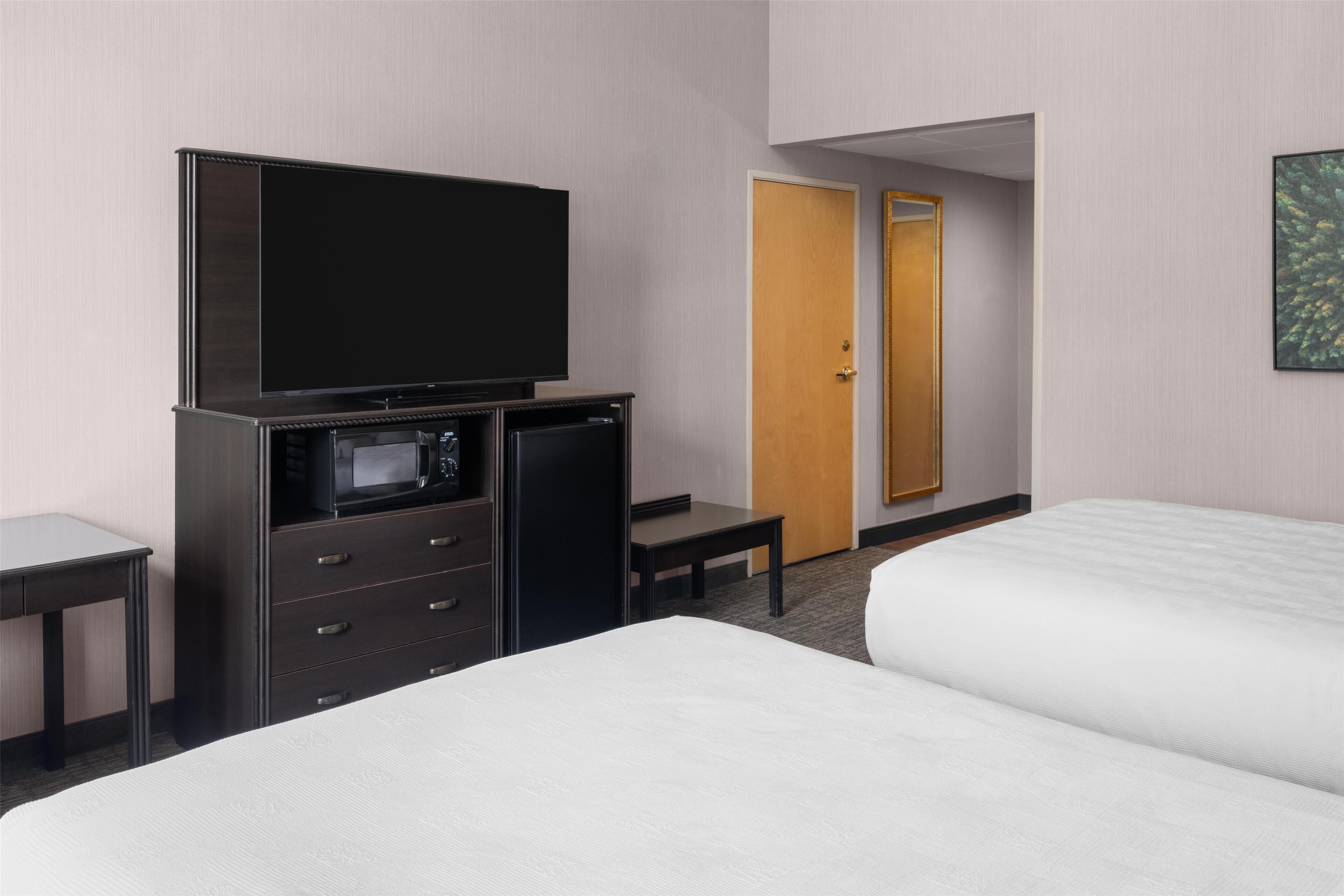 A hotel room with a bed, a TV, a microwave, a desk, and a door.