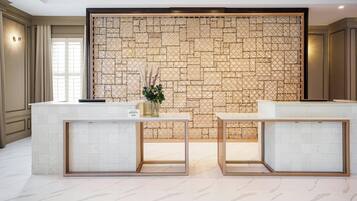 Un área de recepción con un fondo de pared de piedra, dos mostradores de recepción y un jarrón con flores.