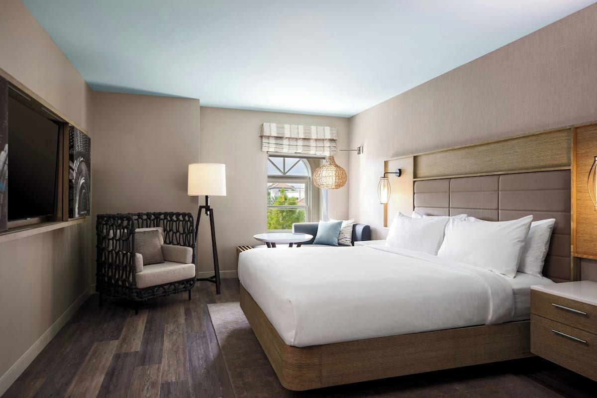 A modern hotel room with a large bed, a small table, a chair, and a TV.