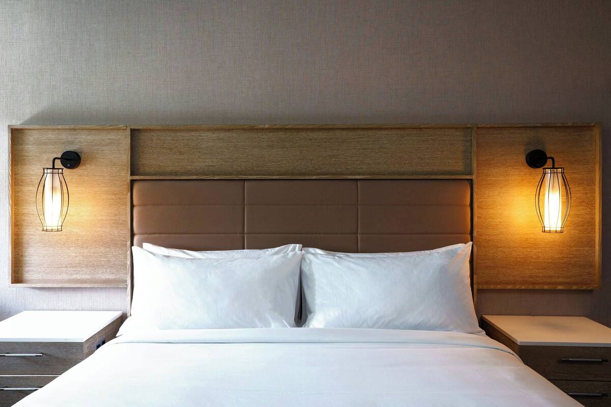 A hotel room with a large bed, two bedside tables, and wall-mounted lamps.