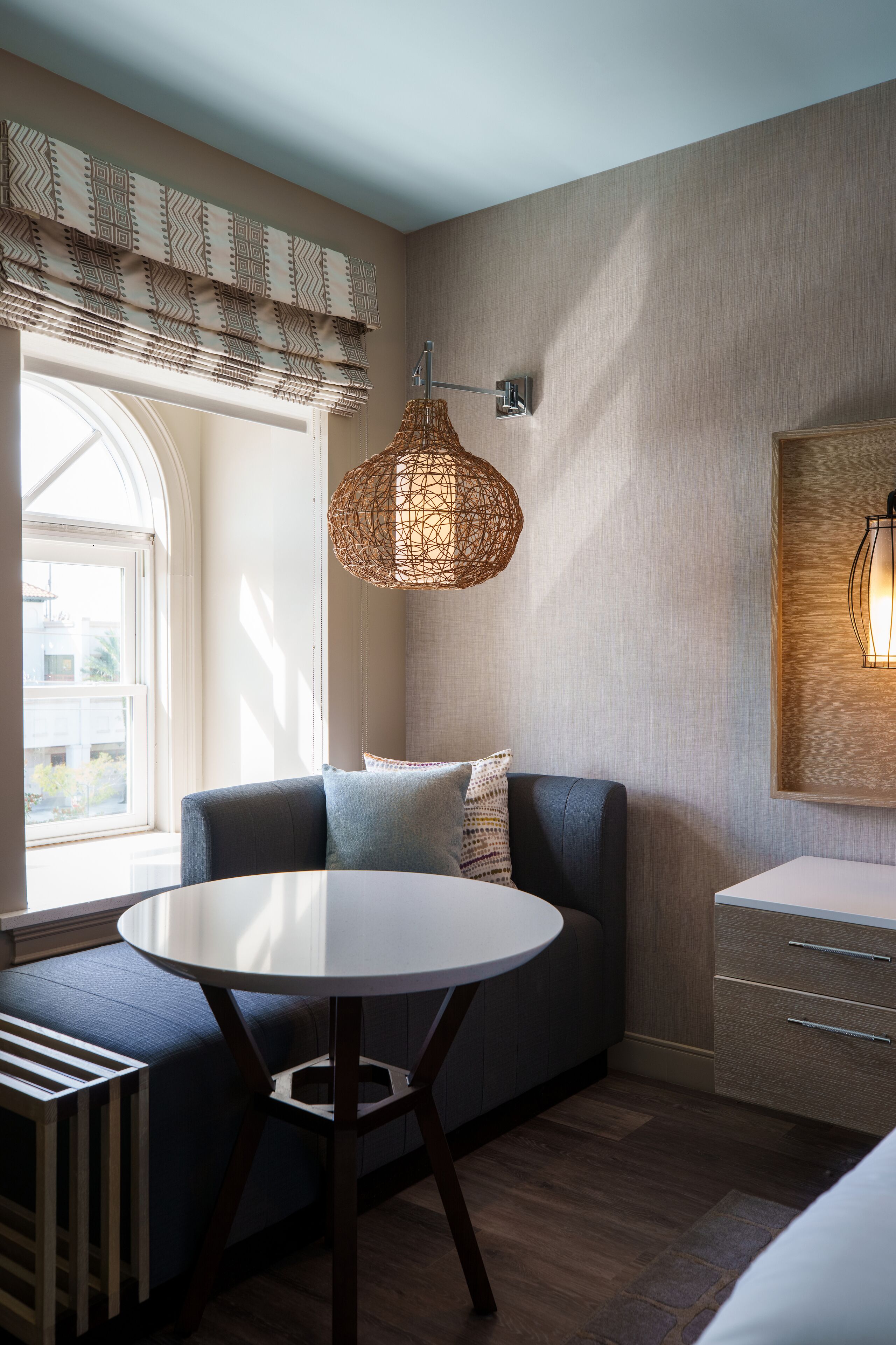 A modern room with a round table, a sofa, and a window with patterned curtains.