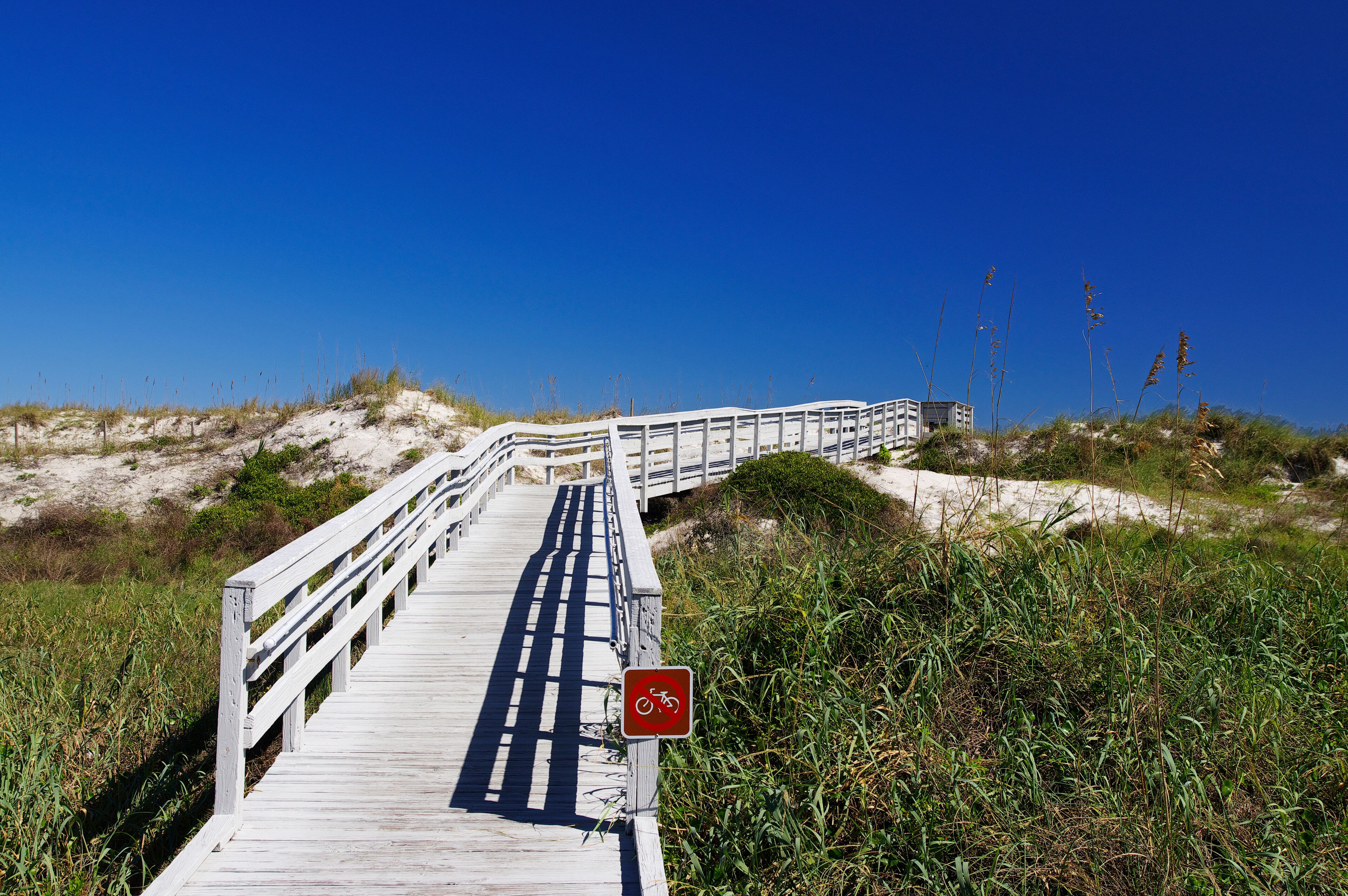 A wooden boardwalk leading to a beach with a red bicycle sign.
