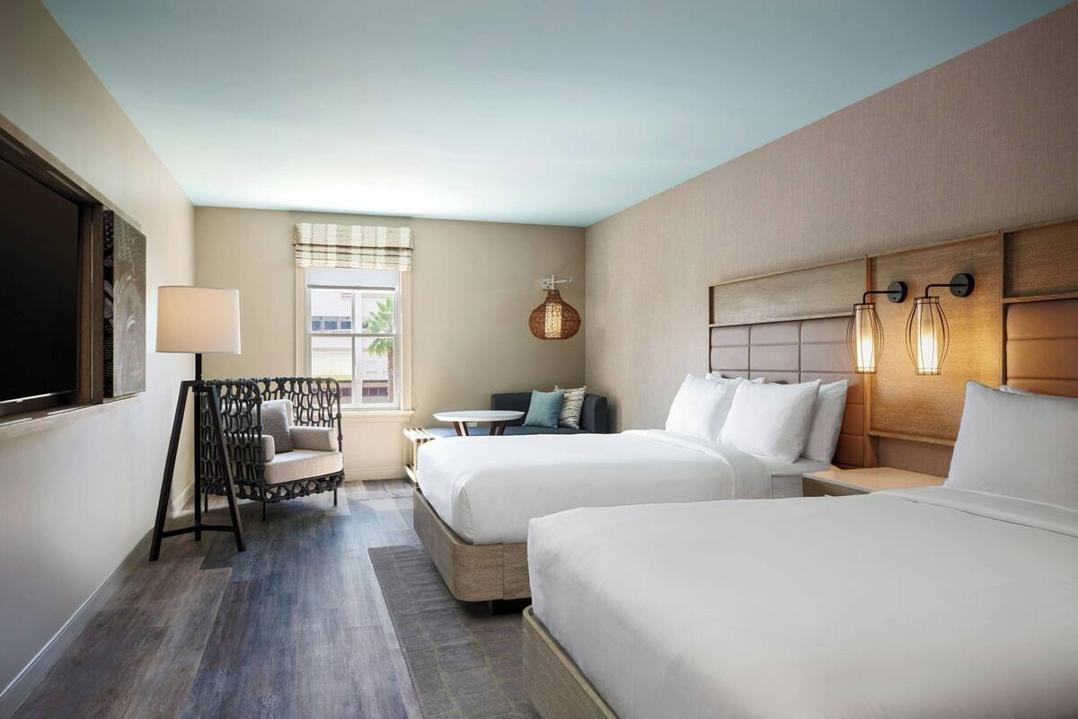 A hotel room with two beds, a seating area, a TV, and a window with curtains.