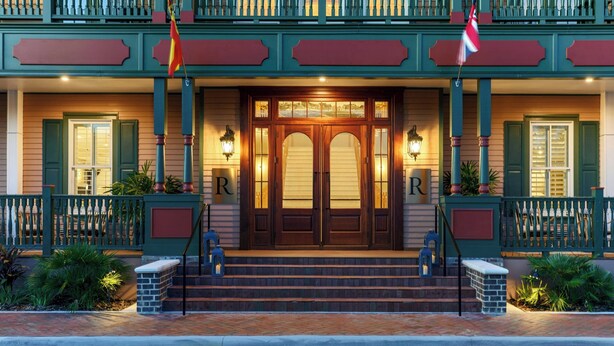 Een hotelentree met een houten dubbele deur, met daaraan twee treden en aan weerszijden een rood-witte vlag.