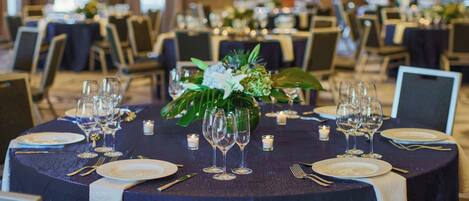 A banquet hall with round tables set for dining, featuring white plates, cutlery, and glassware.