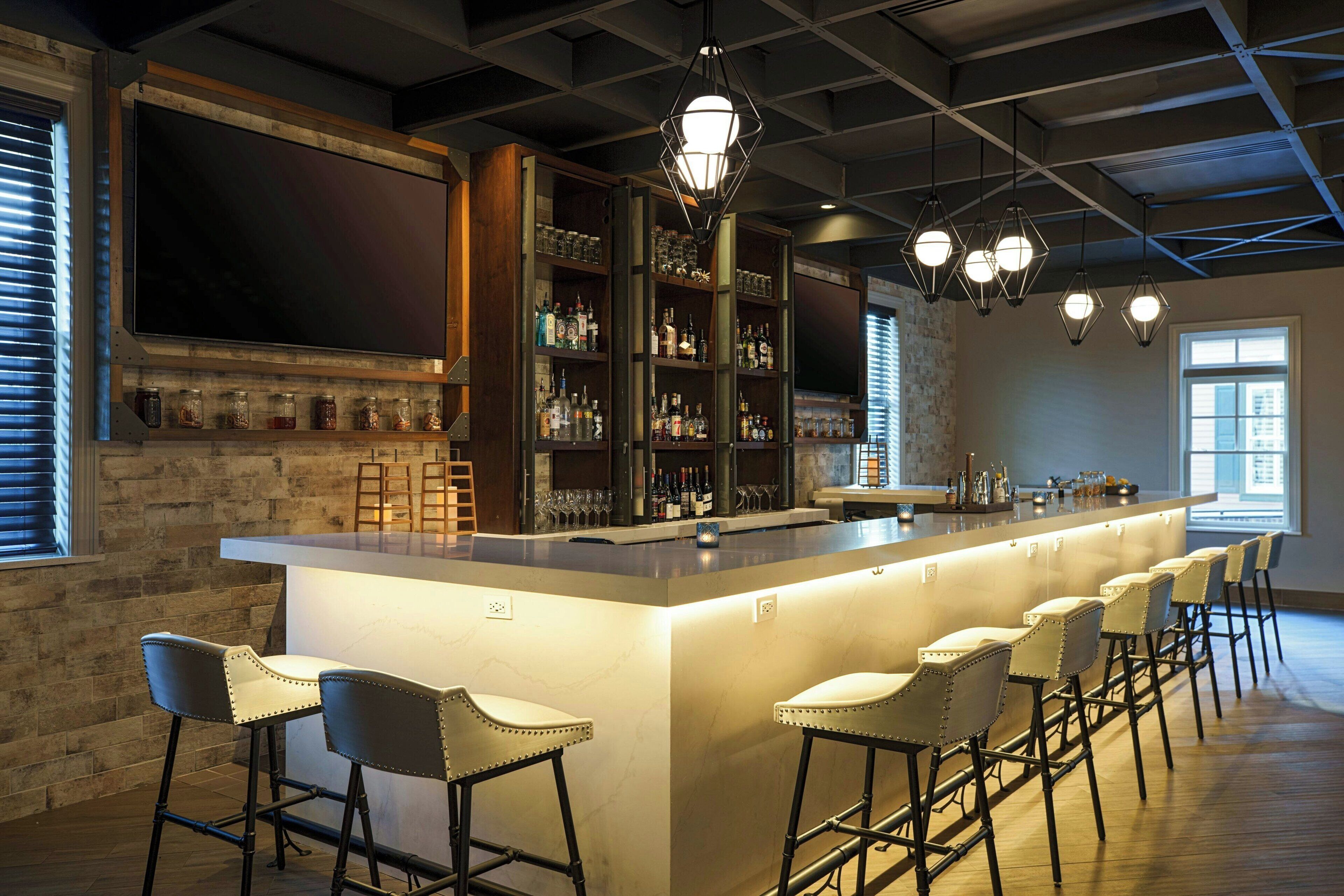 A bar area with a long counter, multiple stools, and shelves stocked with bottles and glasses.