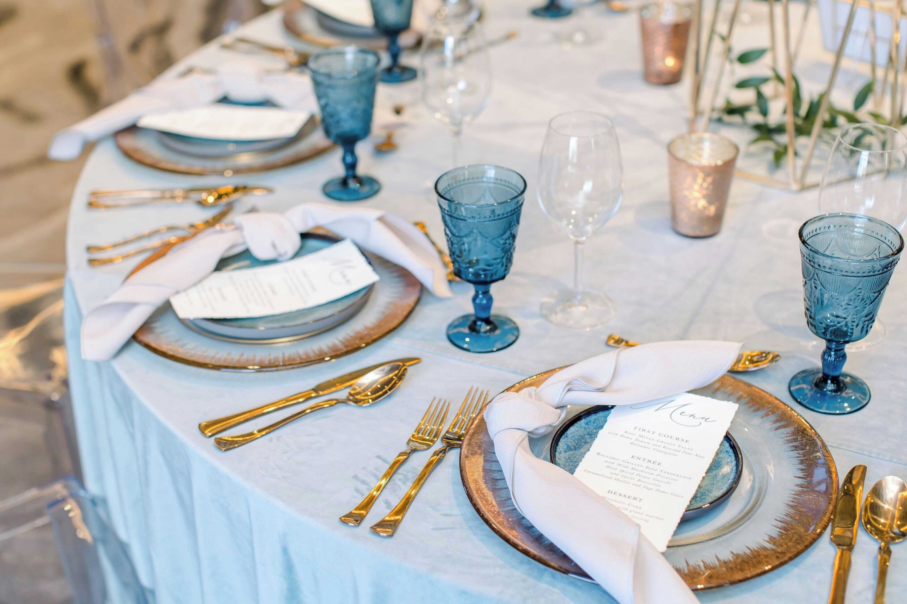 A table set with blue glassware, gold cutlery, and a menu card.