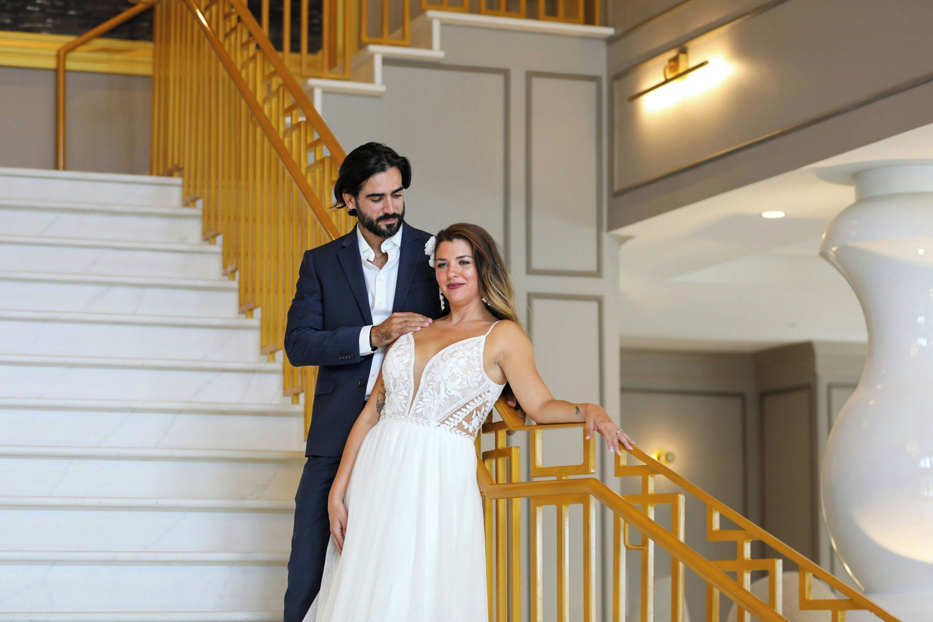 Un couple se trouve sur un escalier dont le sol est en marbre blanc et les rampes en bois.