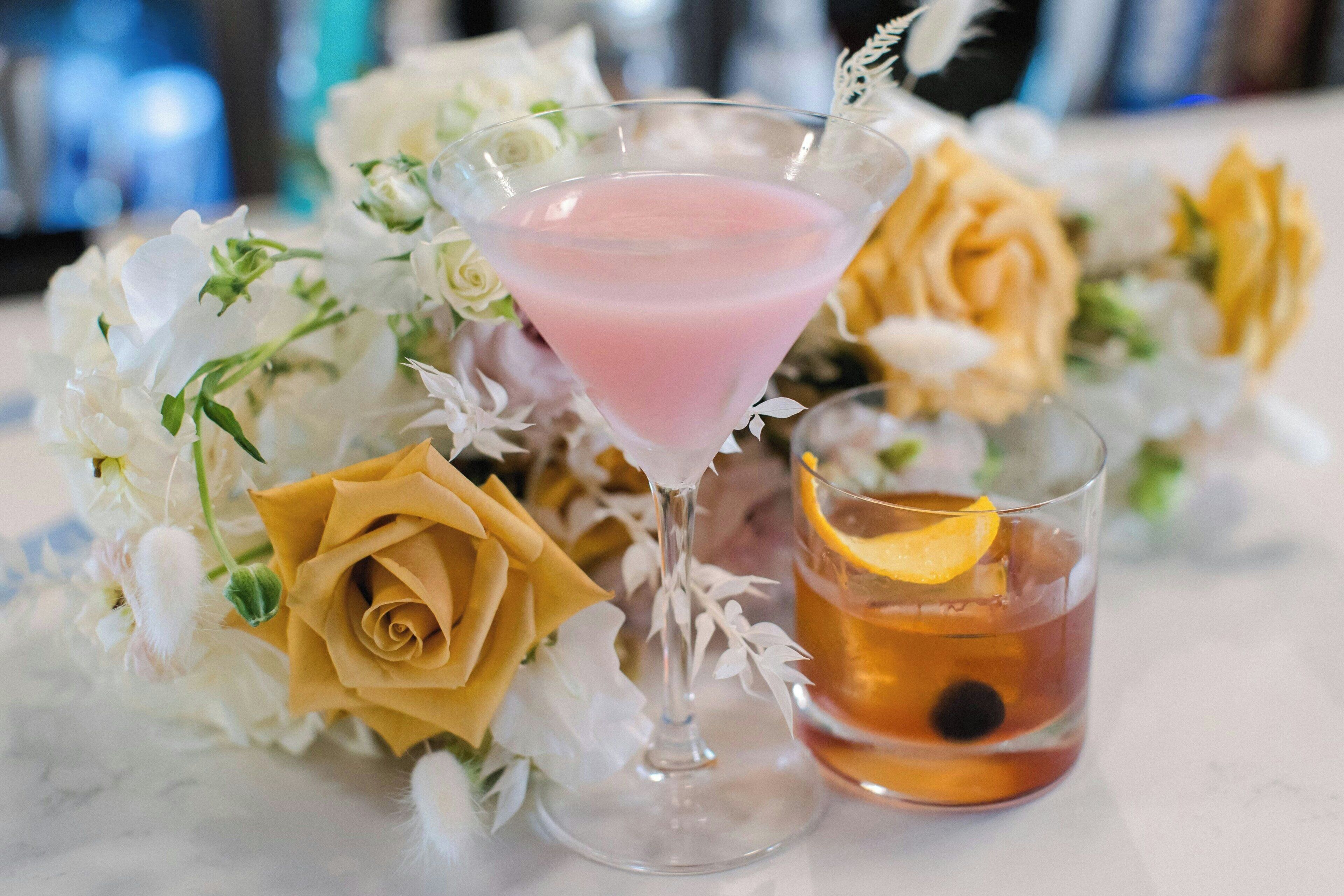 A martini glass with a pink drink and a cocktail glass with an orange slice.