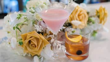 A martini glass with a pink drink and a cocktail glass with an orange slice.