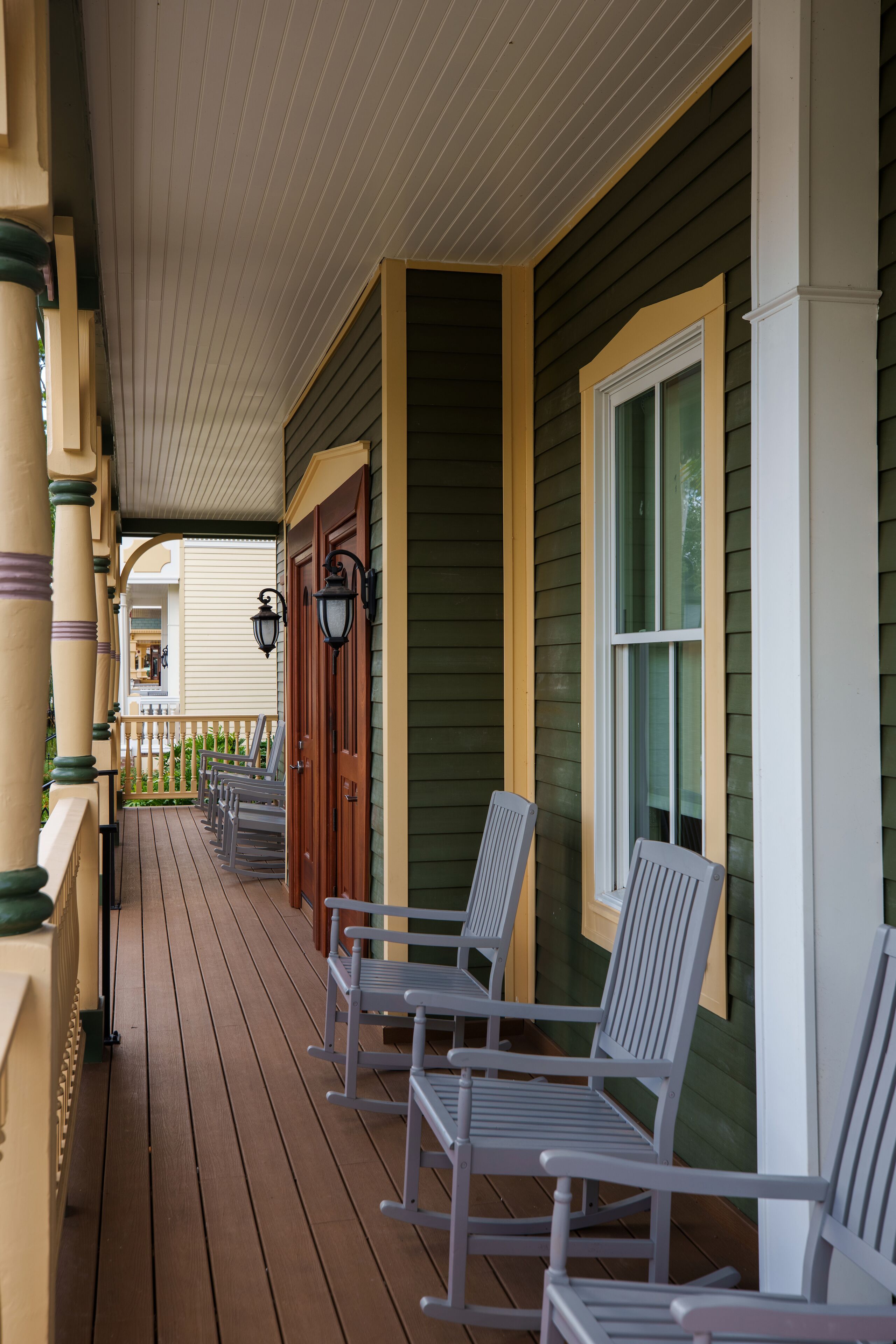 A porch with wooden chairs and a railing, a window, and a door.