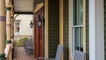 A porch with wooden chairs and a railing, a window, and a door.