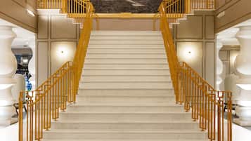 Eine imposante Treppe mit Marmorstufen und goldenen Geländern, die zu einem Balkon mit Blick auf die Stadt führt.