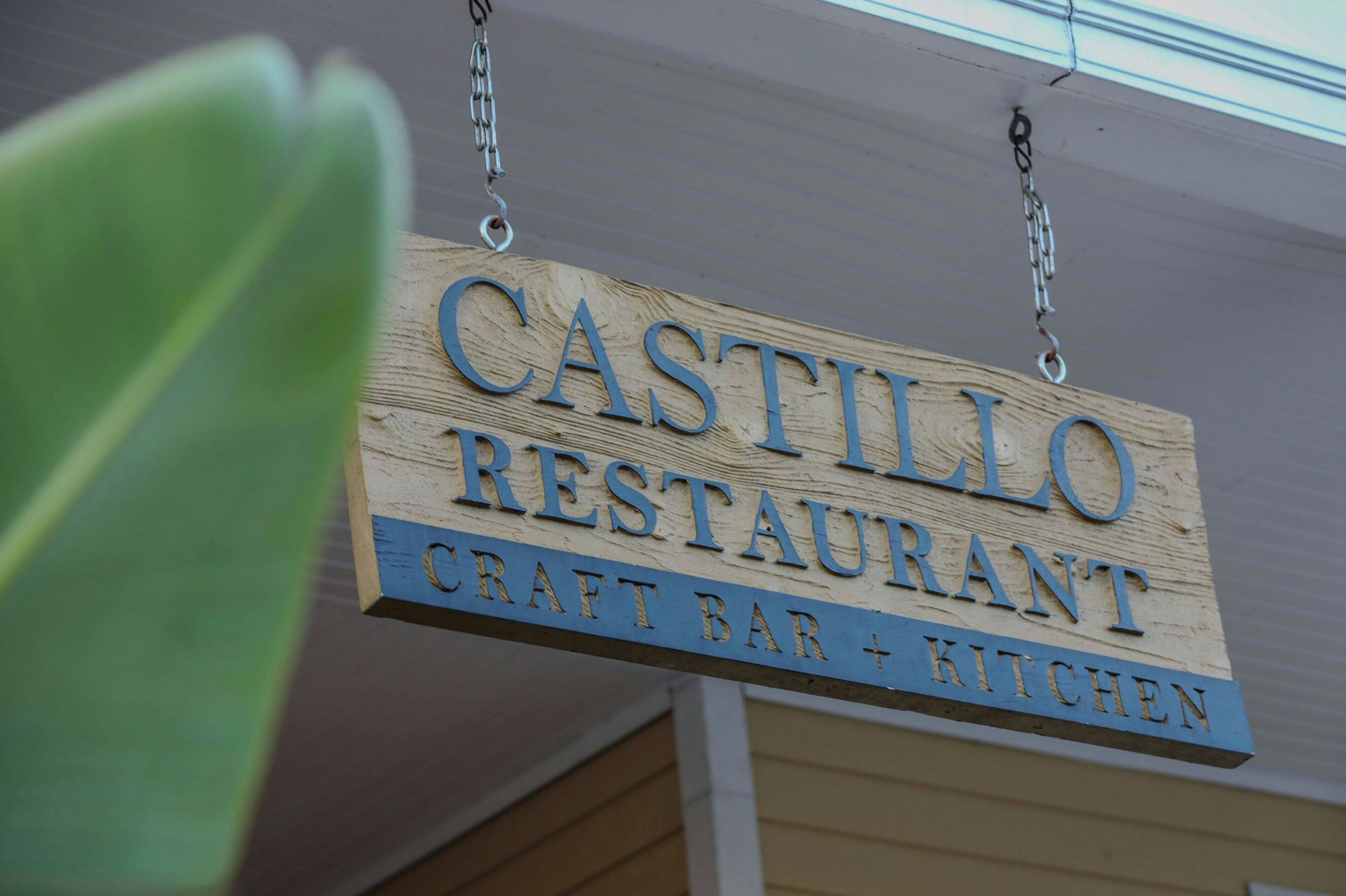 Une enseigne en bois indiquant le restaurant Castillo, avec la mention qu’il dispose d’un bar et d’une cuisine proposant des plats faits maison.