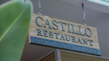 Une enseigne en bois indiquant le restaurant Castillo, avec la mention qu’il dispose d’un bar et d’une cuisine proposant des plats faits maison.