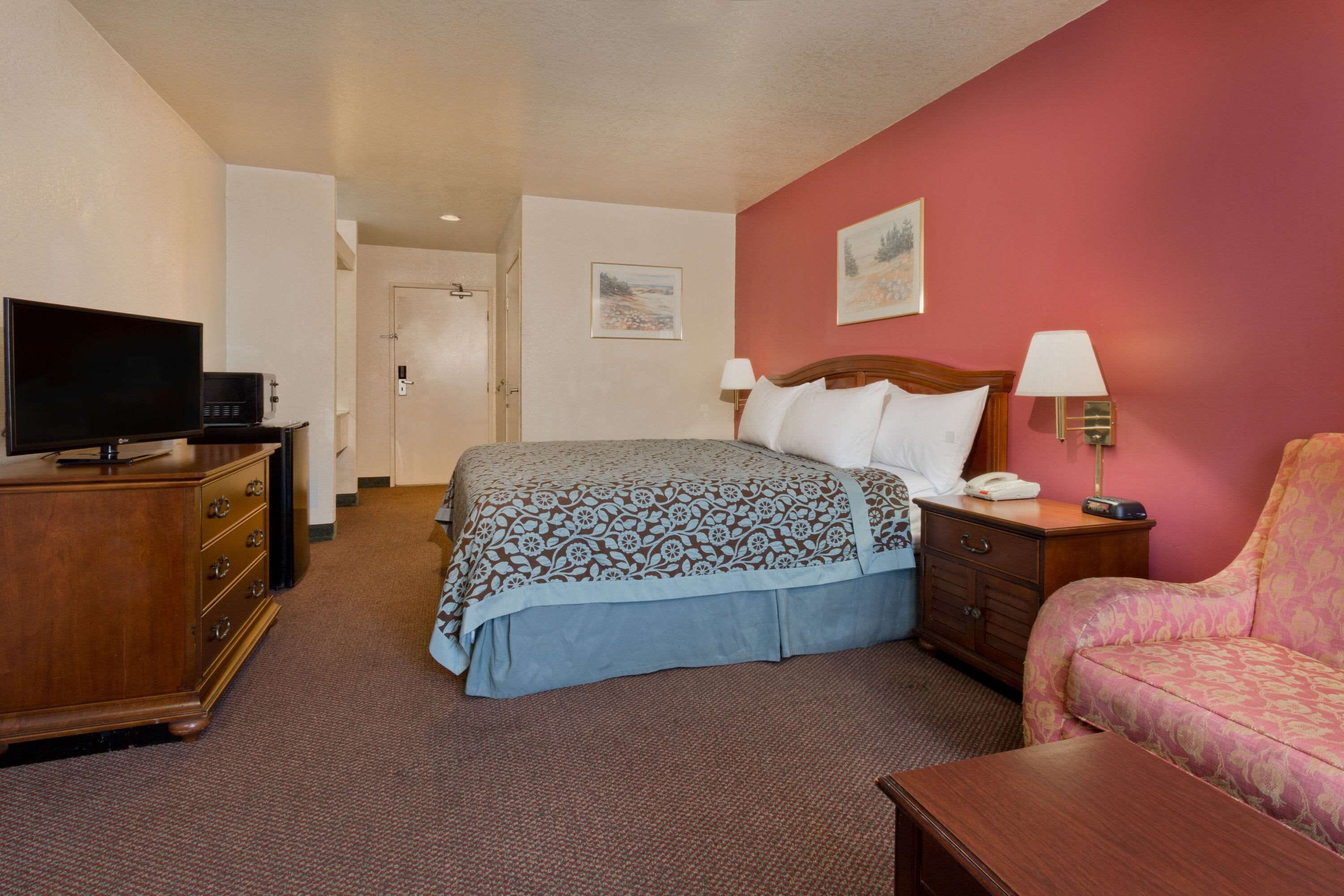 A hotel room with a bed, a television, a dresser, a chair, and a nightstand with a lamp.