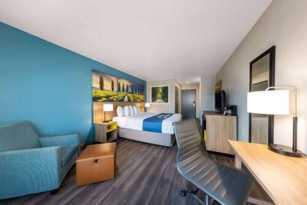 Hotellihuone, jossa on sänky, työpöytä, tuoli, televisio ja taulu seinällä.